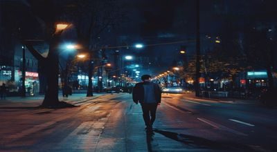 夜晚城市街道上独行的年轻男性，路灯昏黄，远处霓虹灯模糊，画面孤独而真实